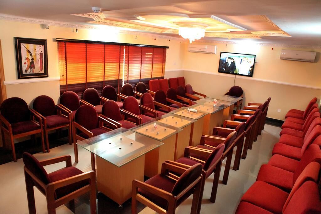 A conference room with a long table and rows of chairs, a television on the wall, and a ceiling light fixture.