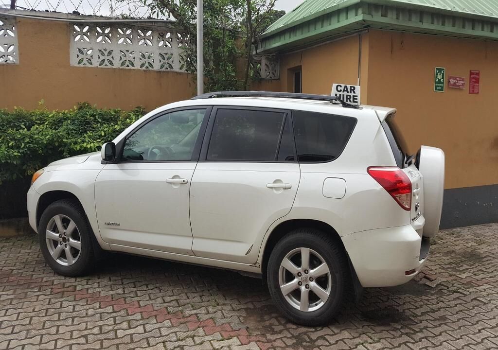 A white SUV parked in front of a building with a 'CAR HIRE' sign.