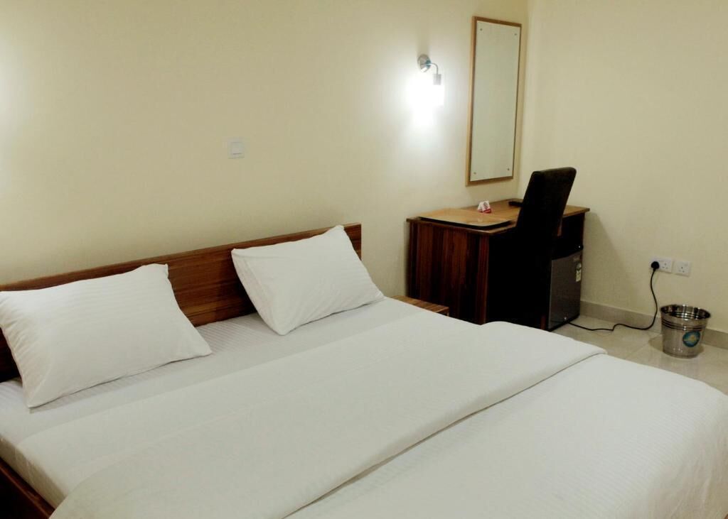 Ein Hotelzimmer mit einem großen Bett, einem Schreibtisch, einem Stuhl, einem Spiegel und einem Mülleimer.