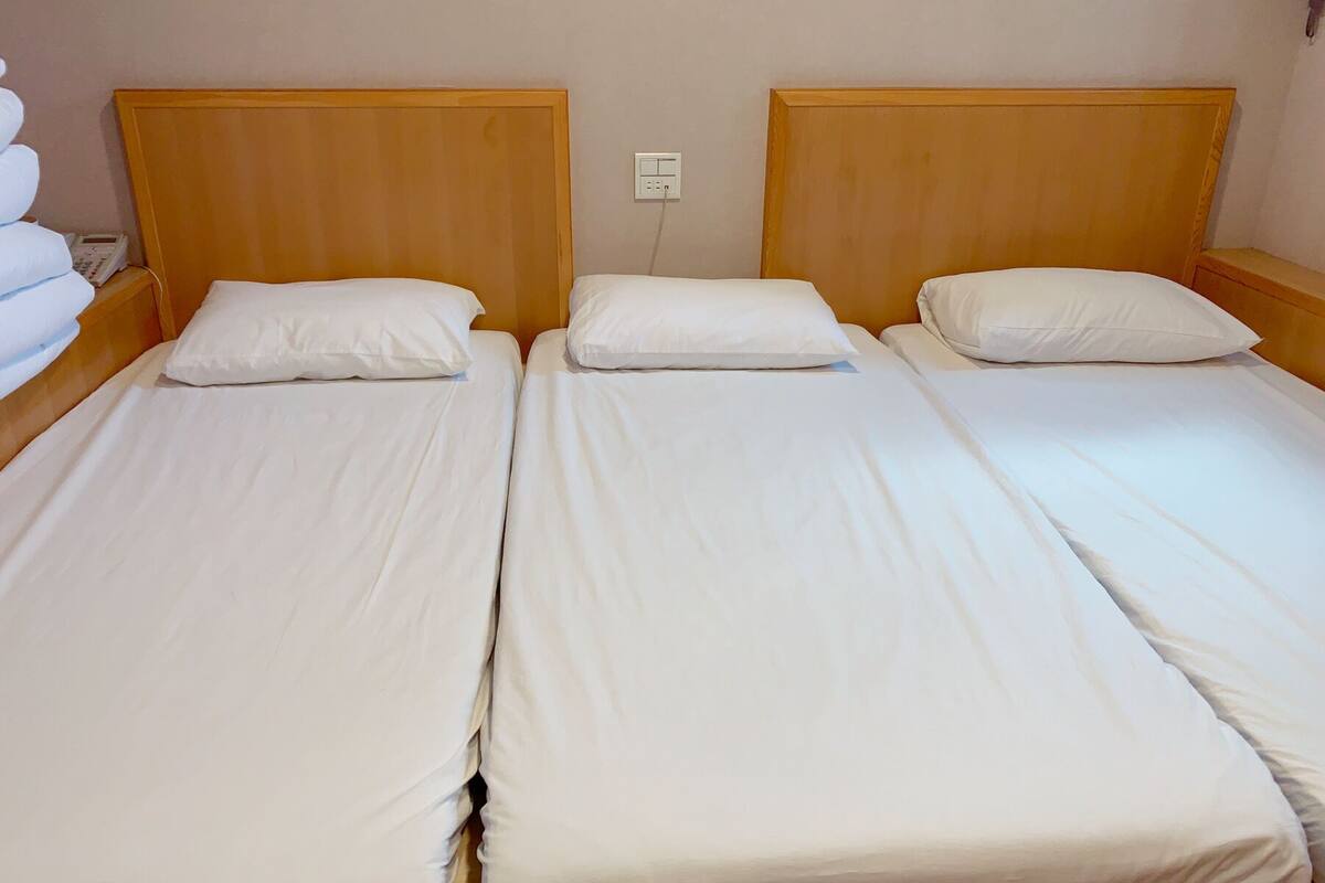 Ein Zimmer mit drei Einzelbetten, jedes mit einem Holz-Kopfteil und weißer Bettwäsche.