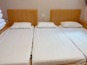 Une chambre avec trois lits simples, chacun doté d’une tête de lit en bois et de draps blancs.