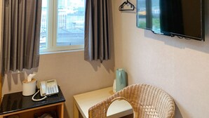 Een hotelkamer met een bed, een bureau met telefoon, een aan de muur bevestigde televisie en een raam met gordijnen.