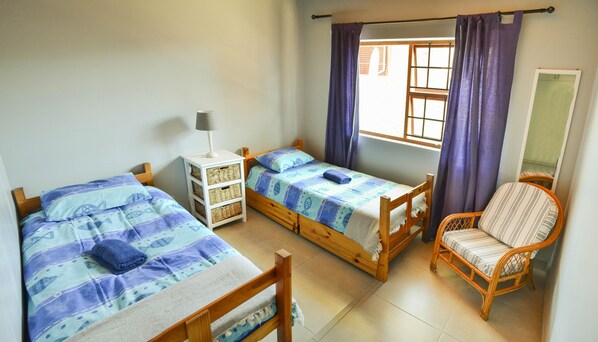 Un dormitorio con dos camas de madera, una mesita de noche, una silla y una ventana con cortinas.