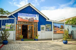 Un restaurante y cafetería con fachada azul, entrada de madera y plantas en macetas.