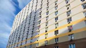 Een meerhoog hotel met een rij balkons, een overdekte parkeerplaats en verschillende geparkeerde auto's.