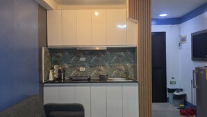 Een moderne woonkamer met een grijze bank, een zwarte salontafel en een keuken met witte kasten en een zwart aanrecht.