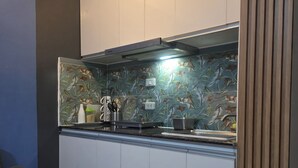 Een kleine keuken met witte kastjes, een decoratieve spatwand en een zwart-wit geruit tapijt.