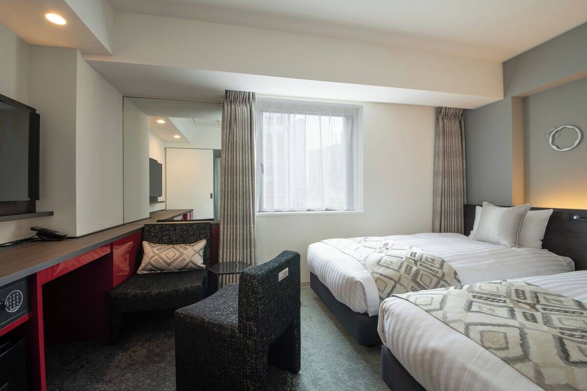 Habitación de hotel con dos camas, un escritorio, una silla, un televisor y una ventana con cortinas.