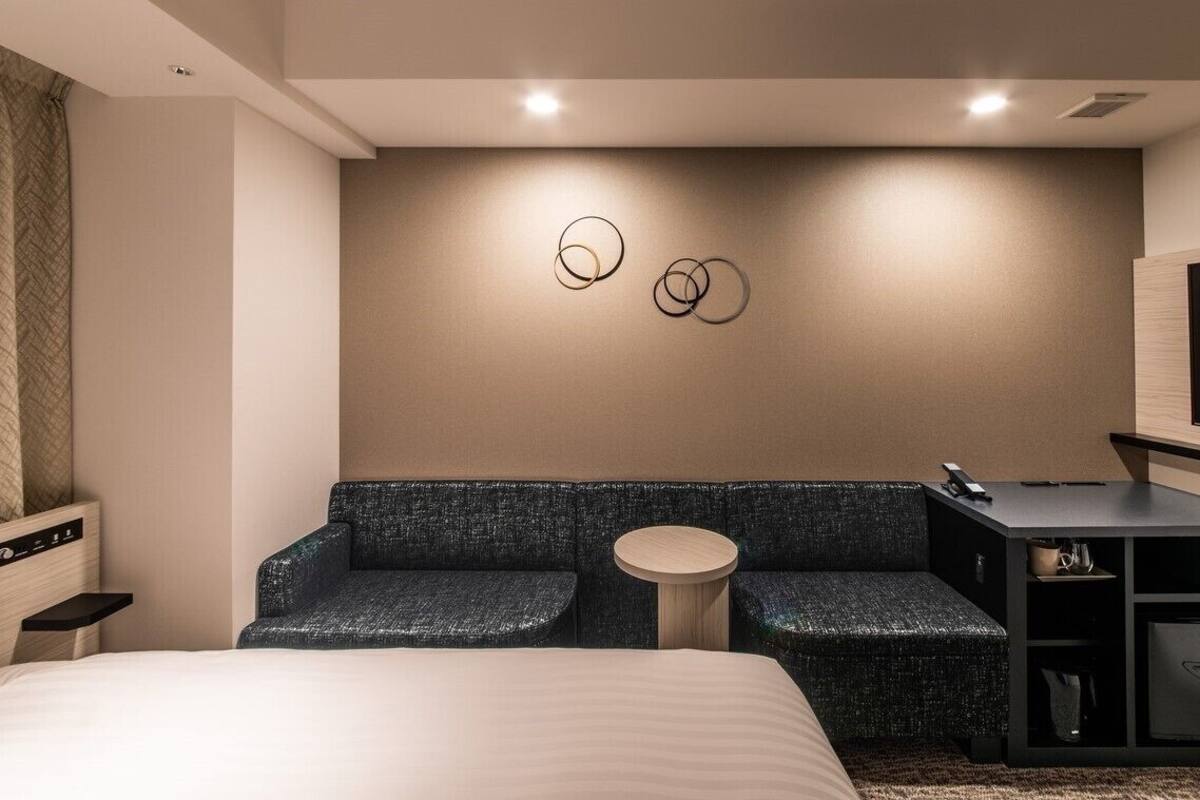 Una habitación de hotel moderna con una cama, una zona de estar con una mesa redonda, un televisor y un minibar.