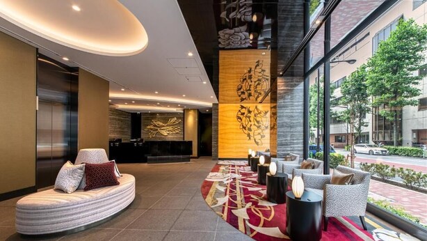 A modern lobby with a curved seating area, a reception desk, and a large window offering a view of the street. - Hotel Vista Tokyo Tsukiji (Tokyo)