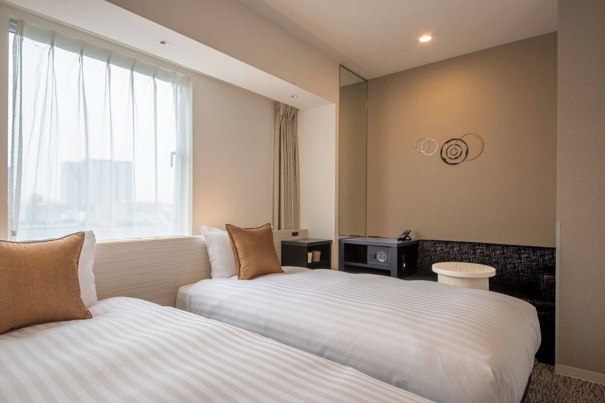 Habitación de hotel con dos camas, un escritorio pequeño, un espejo y vistas a la ciudad.