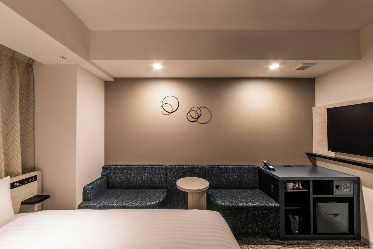 Una habitación de hotel moderna con cama, sofá, una mesita redonda y televisión.