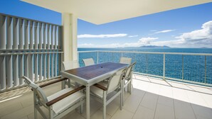 Un balcon avec une table et des chaises, donnant sur une étendue d’eau et sur une terre lointaine.