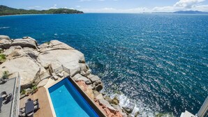 Une piscine offrant une vue sur l’océan, entourée de rochers et d’une petite île au loin.