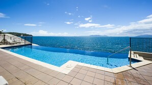 Une piscine à l’eau d’un bleu cristallin, une terrasse carrelée et une vue sur la mer et les montagnes lointaines.