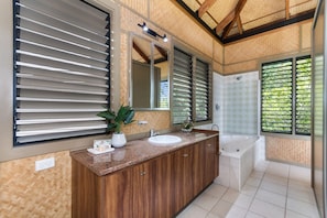 A modern bathroom with a wooden vanity, a large mirror, and a bathtub.