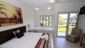 A hotel room with a large bed, a balcony with a chair, a painting on the wall, and a view of the outdoors. - Beachside Apartment 5 (Nelly Bay)