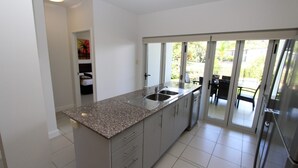 A modern kitchen with granite countertops, stainless steel appliances, and a sliding glass door leading to a balcony. - Beachside Apartment 5 (Nelly Bay)