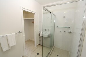Uma casa de banho moderna com cabine de duche em vidro, lavatório branco e closet espaçoso.