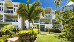 A multi-story residential building with balconies, surrounded by well-maintained greenery and a clear sky. - Beachside Apartment 5 (Nelly Bay)