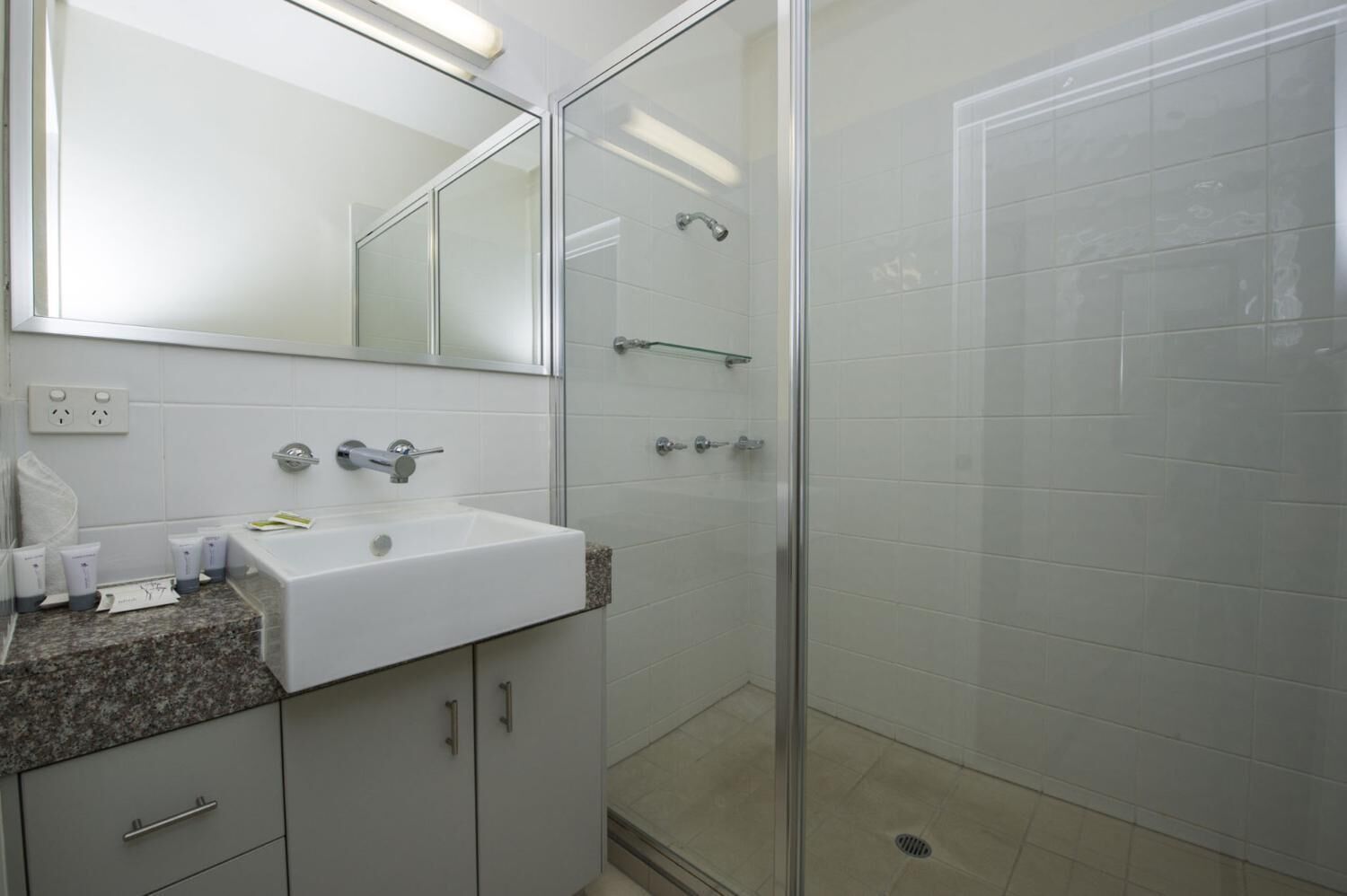 Een moderne badkamer met een wit wastafelmeubel, een granieten aanrechtblad en een douchecabine van glas.