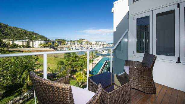 A balcony with wicker furniture overlooking a marina and a swimming pool. - Beachside Apartment 10 (Nelly Bay)