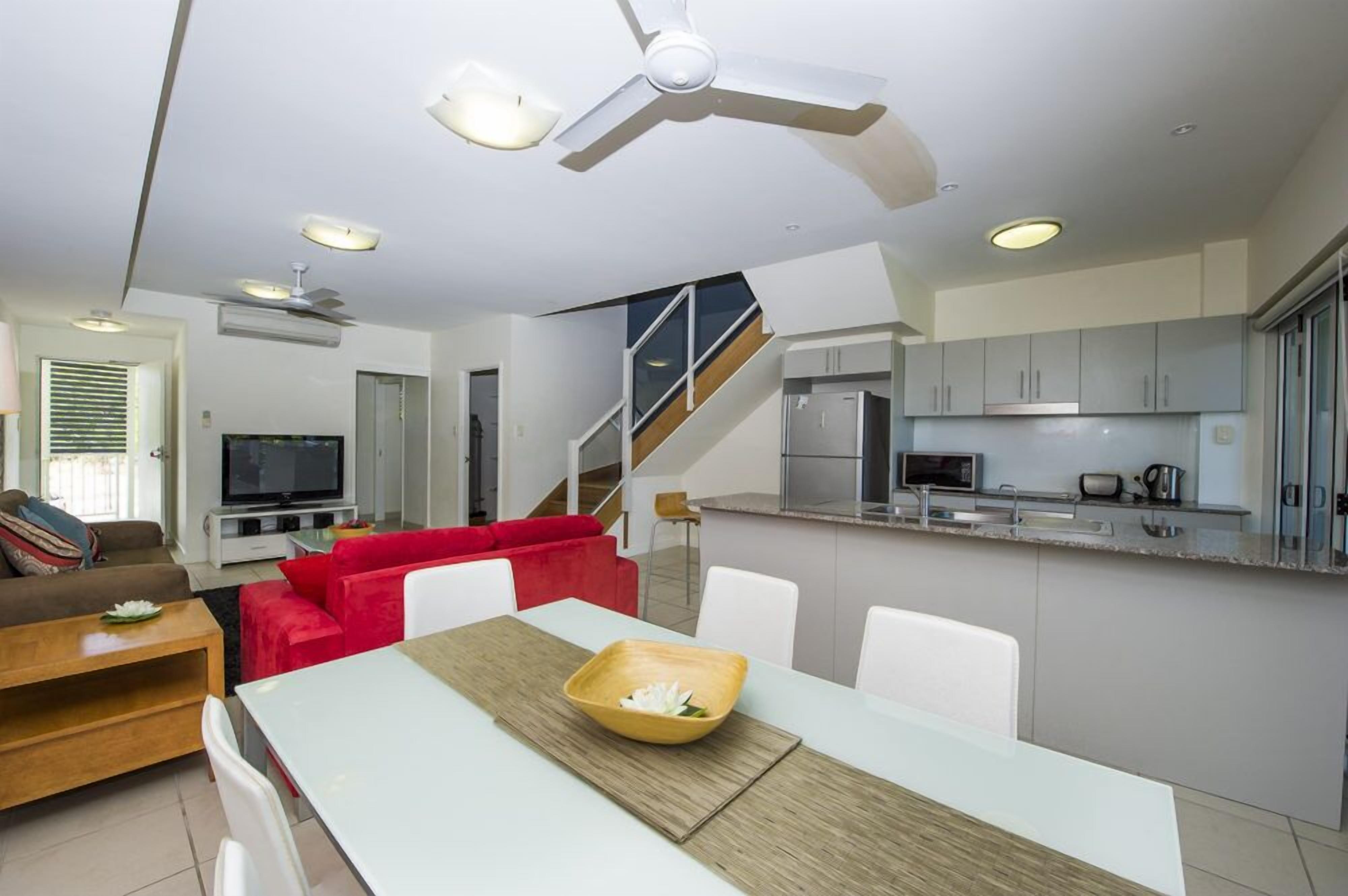 A modern living room with a dining area, a kitchen, and a staircase.