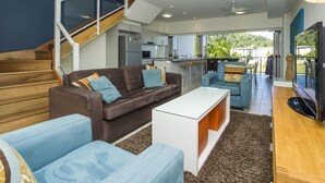 A modern living room with a brown sofa, blue armchairs, a white coffee table, and a TV. - Beachside Apartment 10 (Nelly Bay)