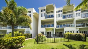 A multi-story hotel with balconies, surrounded by well-maintained lawns and palm trees. - Beachside Apartment 10 (Nelly Bay)