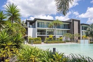A modern hotel with a pool, surrounded by tropical plants and a clear sky. - Blue on Blue Apartment 1015 (Nelly Bay)