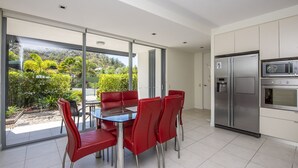 A modern kitchen with a large sliding glass door leading to a balcony, stainless steel appliances, and red dining chairs. - Blue on Blue Apartment 1015 (Nelly Bay)