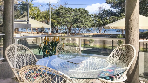 A round glass table with wicker chairs, surrounded by a railing and trees. - Champagne Apartment 1 (Arcadia)