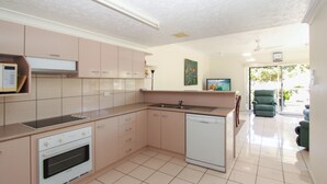 A modern kitchen with a dishwasher, oven, and a built-in microwave. There is a dining area with a green chair and a table. - Champagne Apartment 1 (Arcadia)