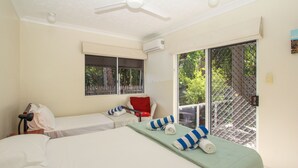 A hotel room with two beds, a window, an air conditioning unit, and a view of greenery outside. - Champagne Apartment 1 (Arcadia)