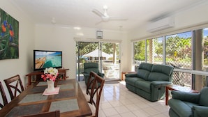 A dining area with a wooden table, chairs, and a vase of flowers. There is a television on the wall and a green sofa in the living area. - Champagne Apartment 1 (Arcadia)