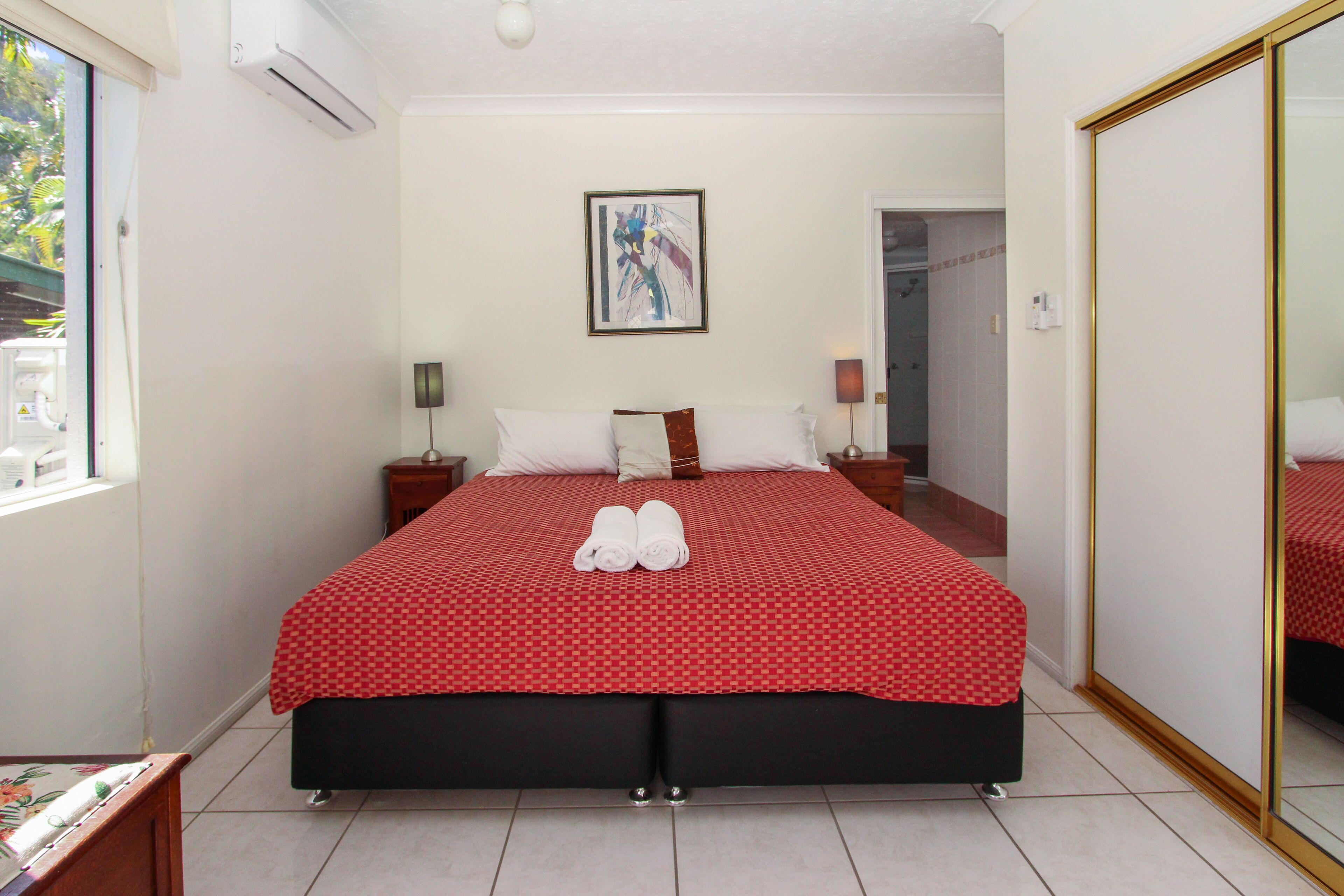 A hotel room with a large bed, a bedside table, a nightstand, a mirror, and a window.