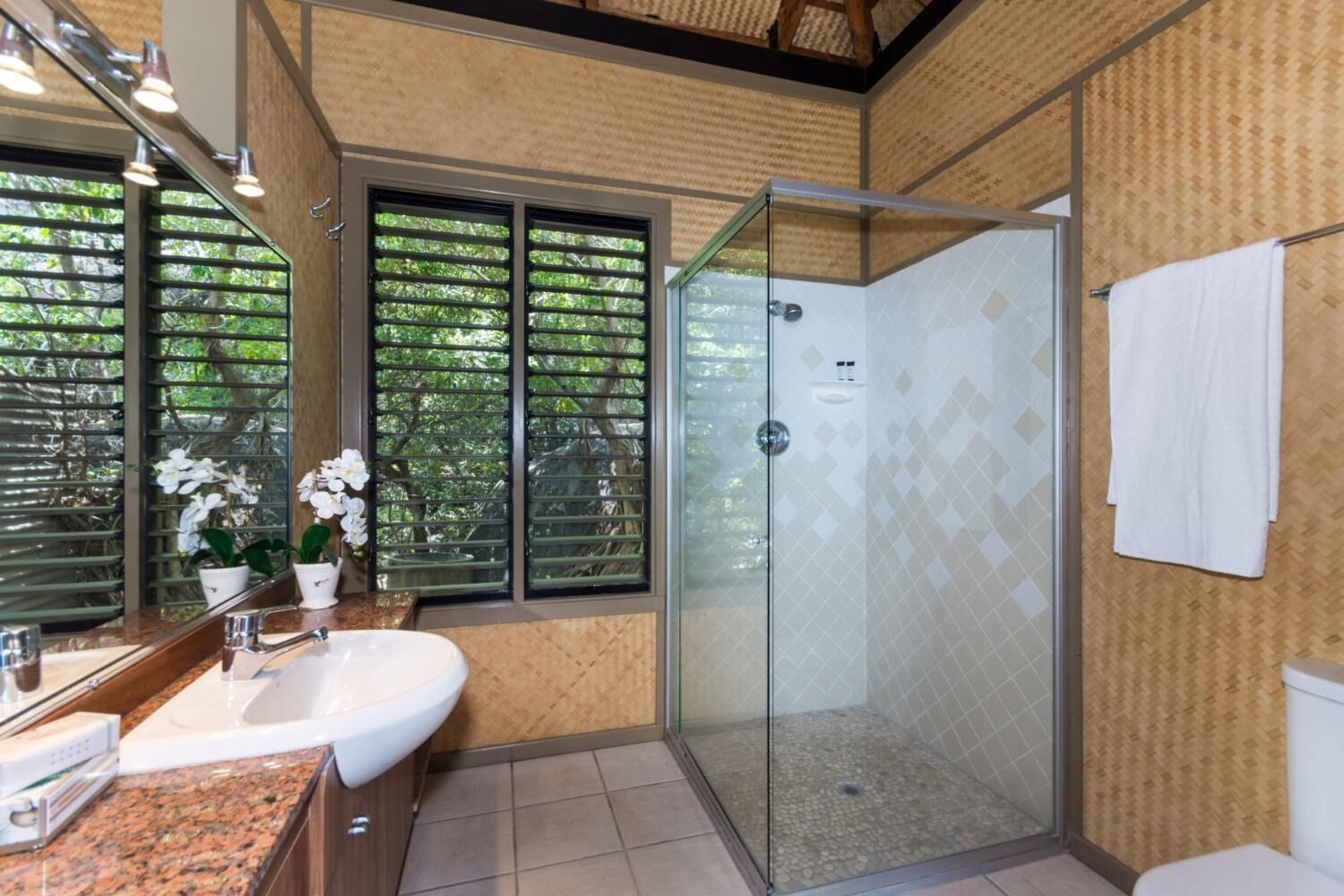 Un bagno con cabina doccia in vetro, lavandino con specchio e finestra con persiane.