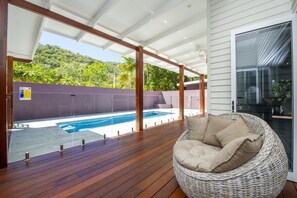 Un espacio al aire libre techado con una terraza de madera, una silla de mimbre y una piscina.