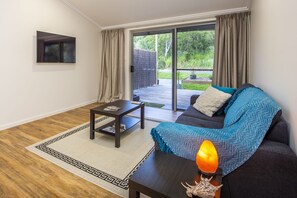 Un salon moderne avec un canapé foncé, une table basse et une vue sur un jardin, visible à travers une porte-fenêtre coulissante.