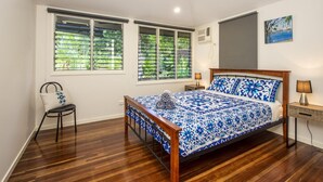A bedroom with a wooden bed, two bedside tables, a chair, and a ceiling fan. - Sail Rock Apartment 1 (Picnic Bay)