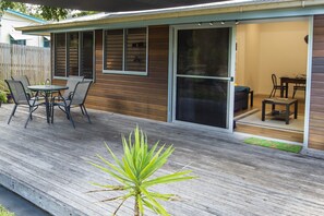 A covered patio with a table and chairs, a sliding glass door leading to an interior space, and a wooden deck. - Sail Rock Apartment 1 (Picnic Bay)