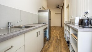 A narrow kitchen with a stainless steel sink, a refrigerator, and a microwave. There is a wooden floor and white cabinetry. - Sail Rock Apartment 1 (Picnic Bay)