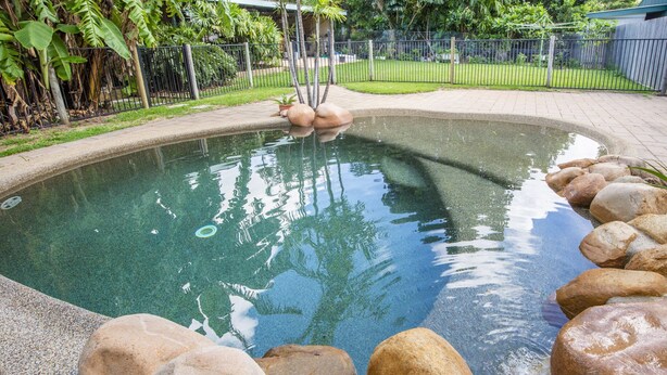 Une piscine à bord incurvé, entourée de gros rochers et d’une clôture métallique.