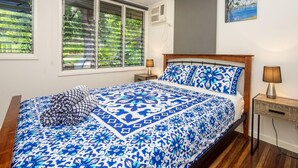 Une chambre avec un grand lit, deux tables de chevet, une fenêtre avec des stores, un tableau au mur et un appareil de climatisation.
