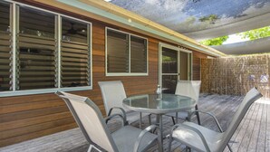 Une terrasse extérieure avec une table ronde et quatre chaises, des murs en bois et un espace abrité doté d’un ventilateur de plafond.