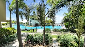 A pool area with a clear blue pool, surrounded by palm trees and a fence. - Blue on Blue Apartment 815 (Nelly Bay)