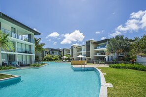 Un hotel moderno con piscina central, varios balcones y exuberante jardinería.