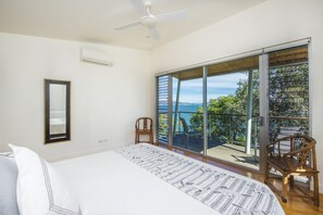 A bedroom with a large bed, a ceiling fan, a sliding glass door leading to a balcony with a view of the sea. - Headland Hideaway (Picnic Bay)