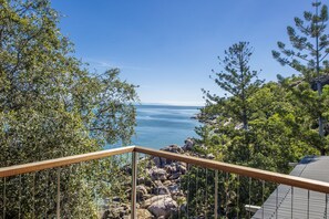 A balcony with a view of the sea, surrounded by trees and rocks. - Headland Hideaway (Picnic Bay)