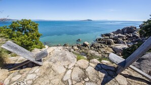 Eine Küstenlandschaft mit klarem, blauem Wasser, felsigem Gelände und einer hölzernen Bank.